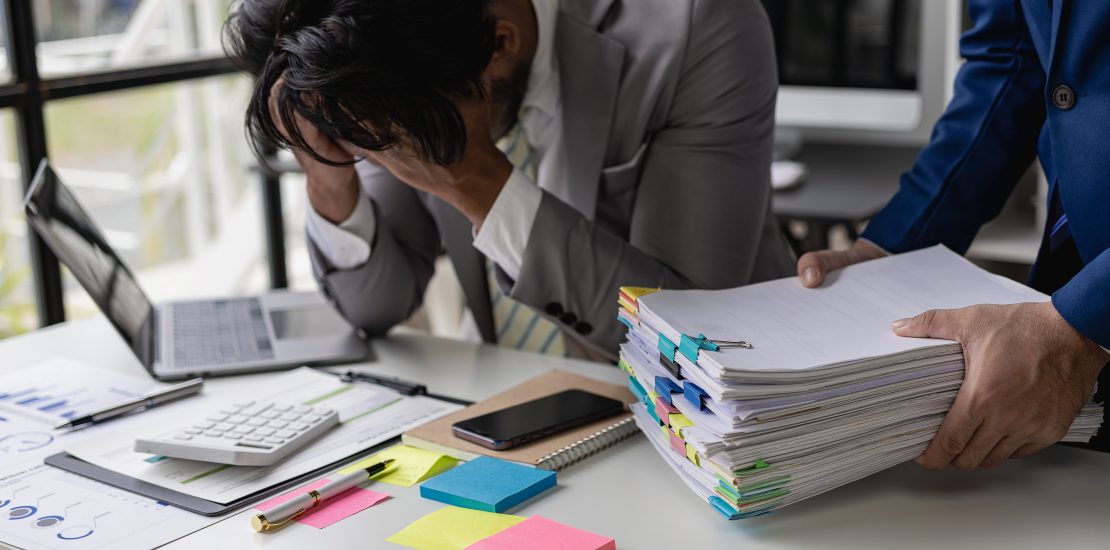 Male office worker, exhausted and burned out from overwork, covers his face.