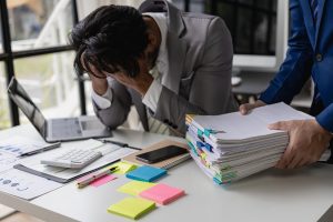 Male office worker, exhausted and burned out from overwork, covers his face.